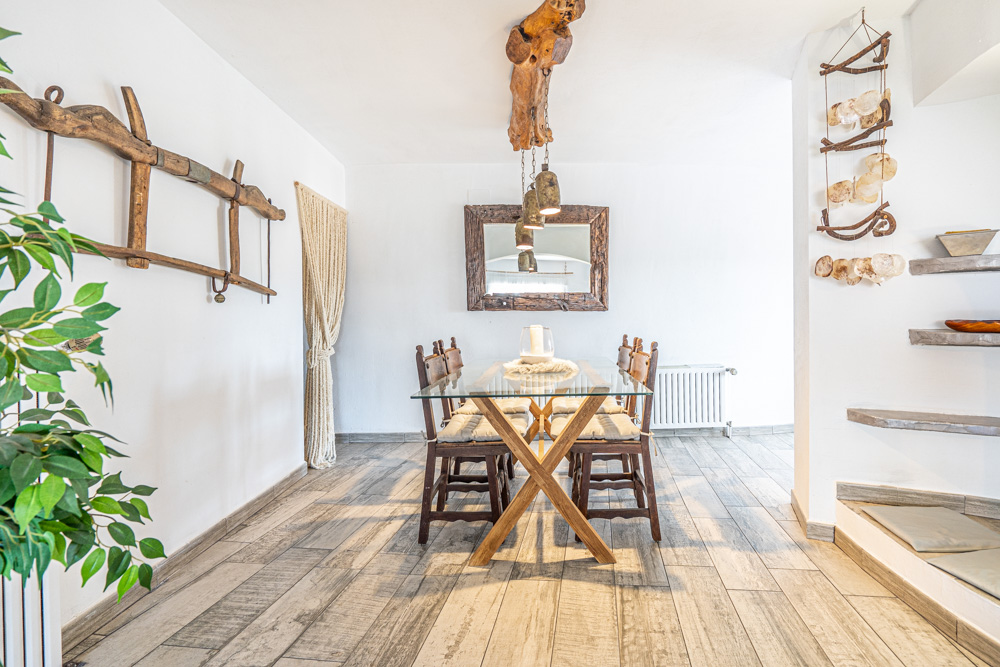 Rustic dining space with a glass-top table and wooden X-frame legs, featuring a unique natural timber light fixture and a large handcrafted wood-framed mirror.