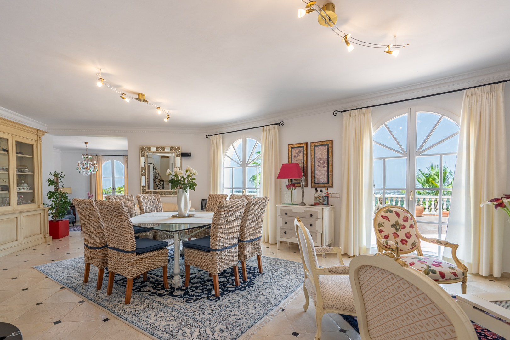 Bright dining area featuring wicker chairs and a glass table, complemented by arched windows that offer direct access to the terrace and natural light.