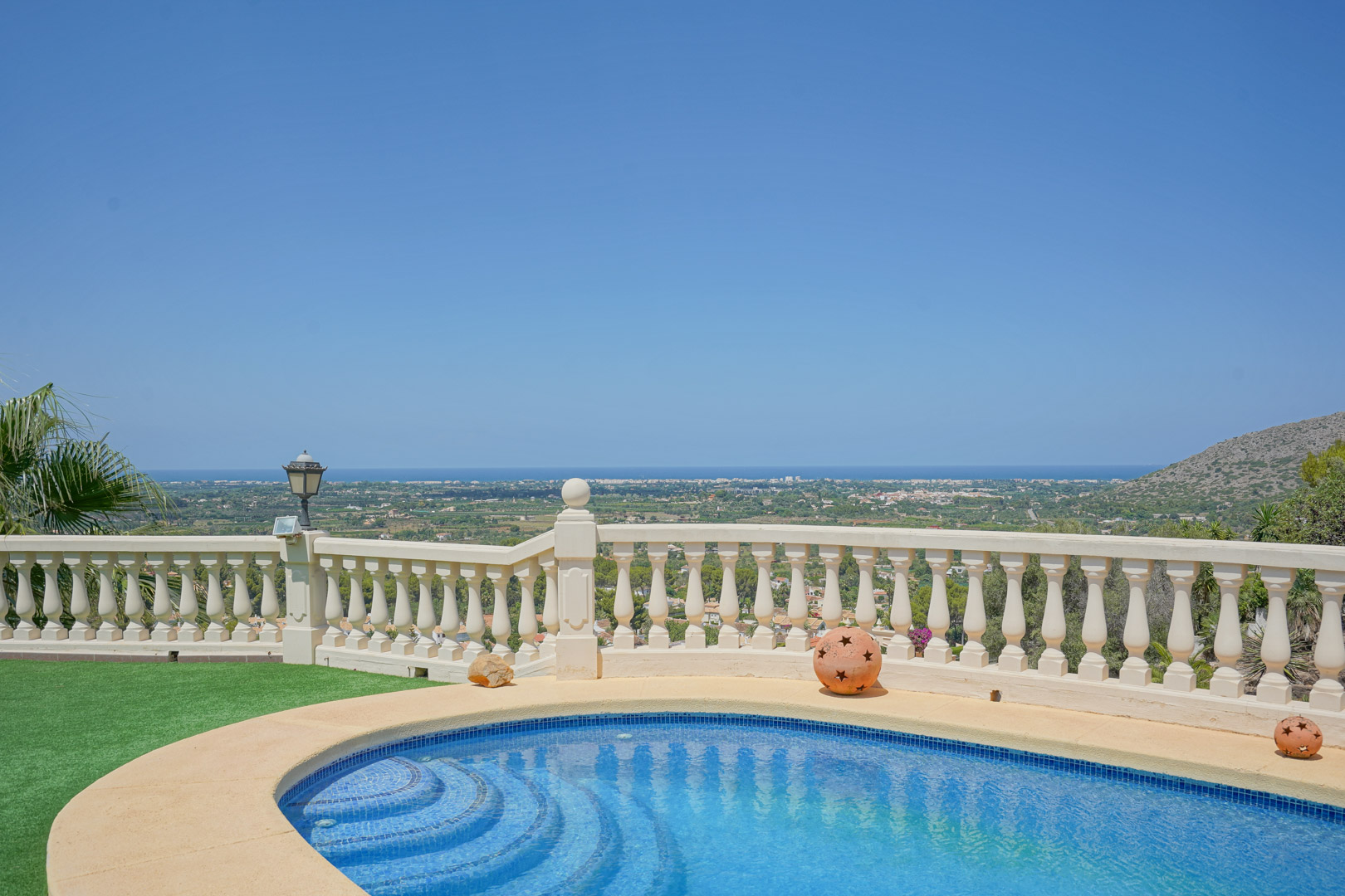 Curved mosaic-tiled pool framed by a classic stone balustrade, offering expansive panoramic views of the Mediterranean coastline and the lush valley.