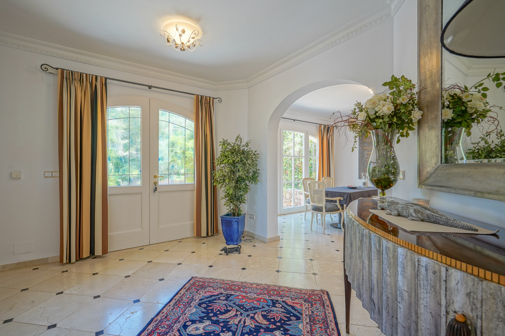 Elegant entrance hall featuring marble flooring with black diamond inserts. An arched doorway leads to the dining area, complemented by white woodwork and natural light.