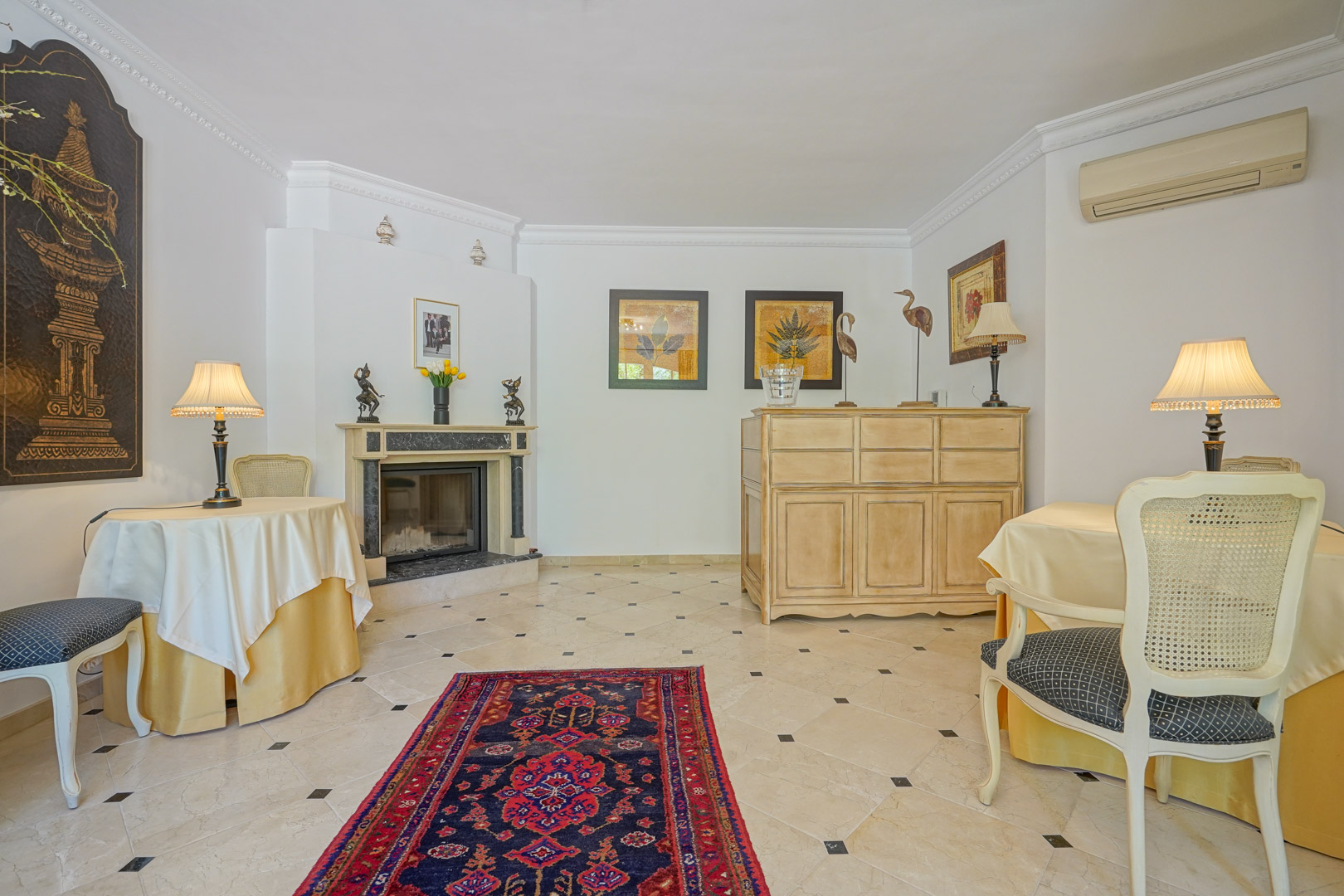 Elegant living area featuring a marble fireplace, ceramic tile flooring with black inserts, and classical furniture accented by a Persian rug.