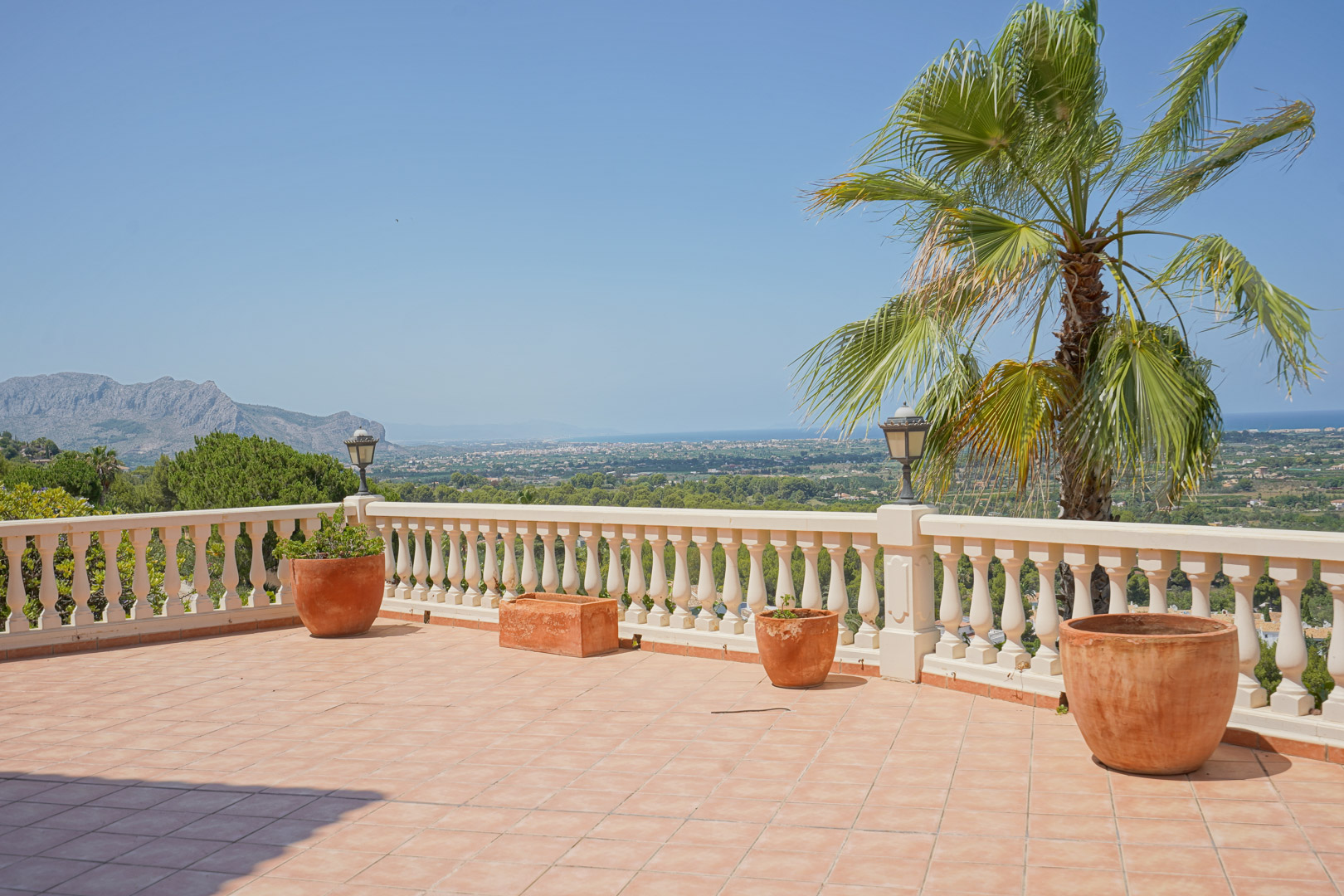 Elevated terrace featuring terracotta tiling and a classic white balustrade, overlooking the Mediterranean coastline and surrounding mountain landscape.