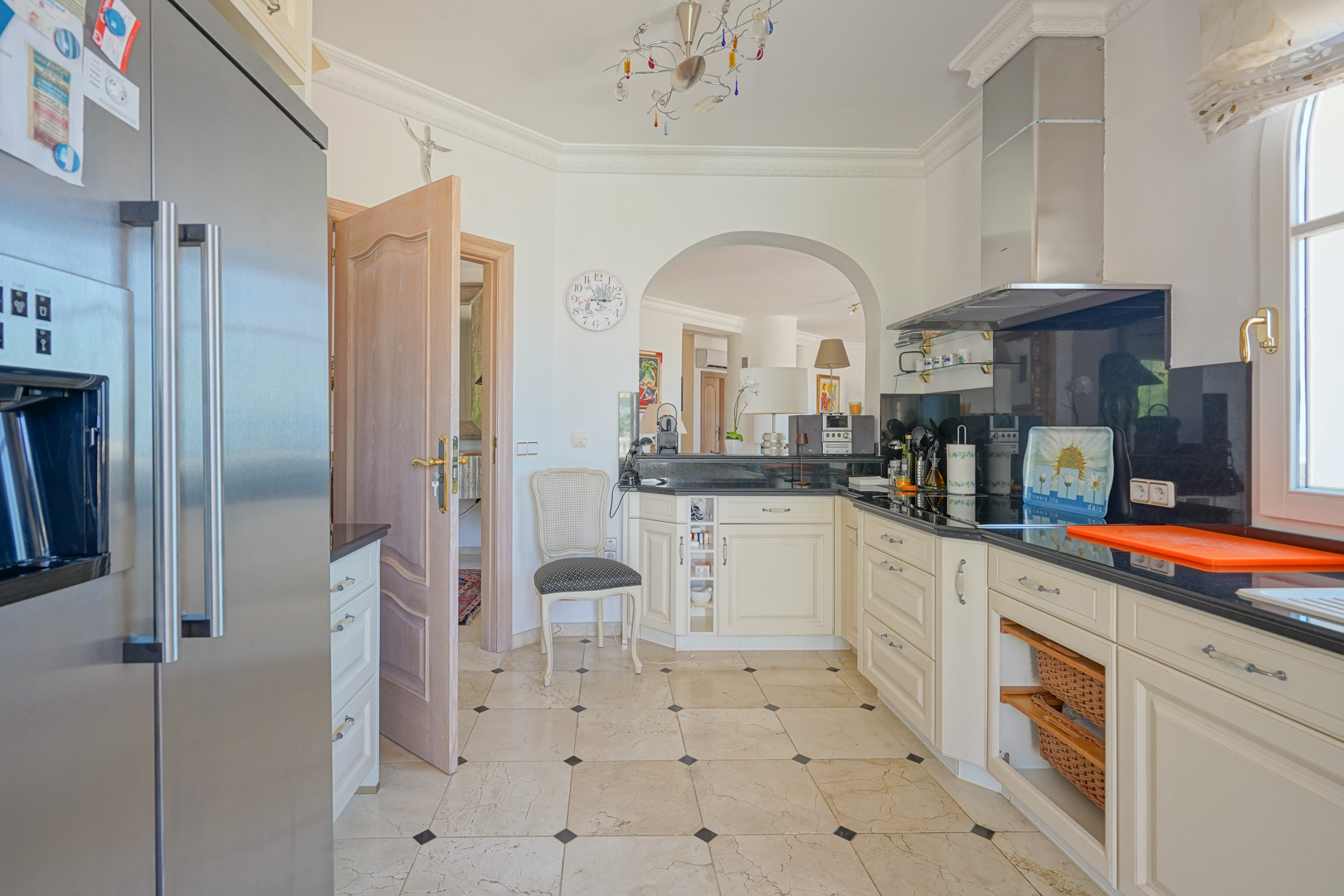 Fully equipped kitchen featuring cream cabinetry, black granite countertops, and marble flooring. The space includes premium stainless steel appliances and an arched opening to the living area.