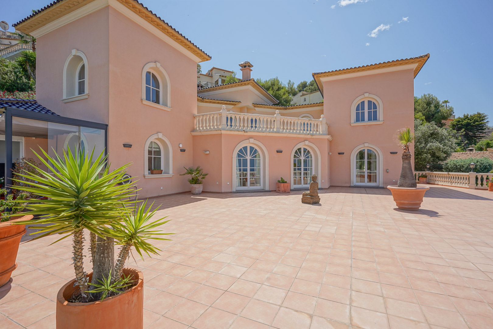 Large outdoor terrace with terracotta tiling, white arched windows, and a salmon-colored facade featuring classic architectural details.