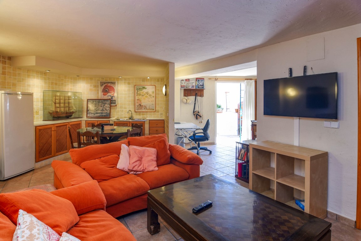 Multi-purpose living area featuring orange sofas, a dedicated office nook, and a secondary kitchen with wooden cabinetry and tiled backsplash.