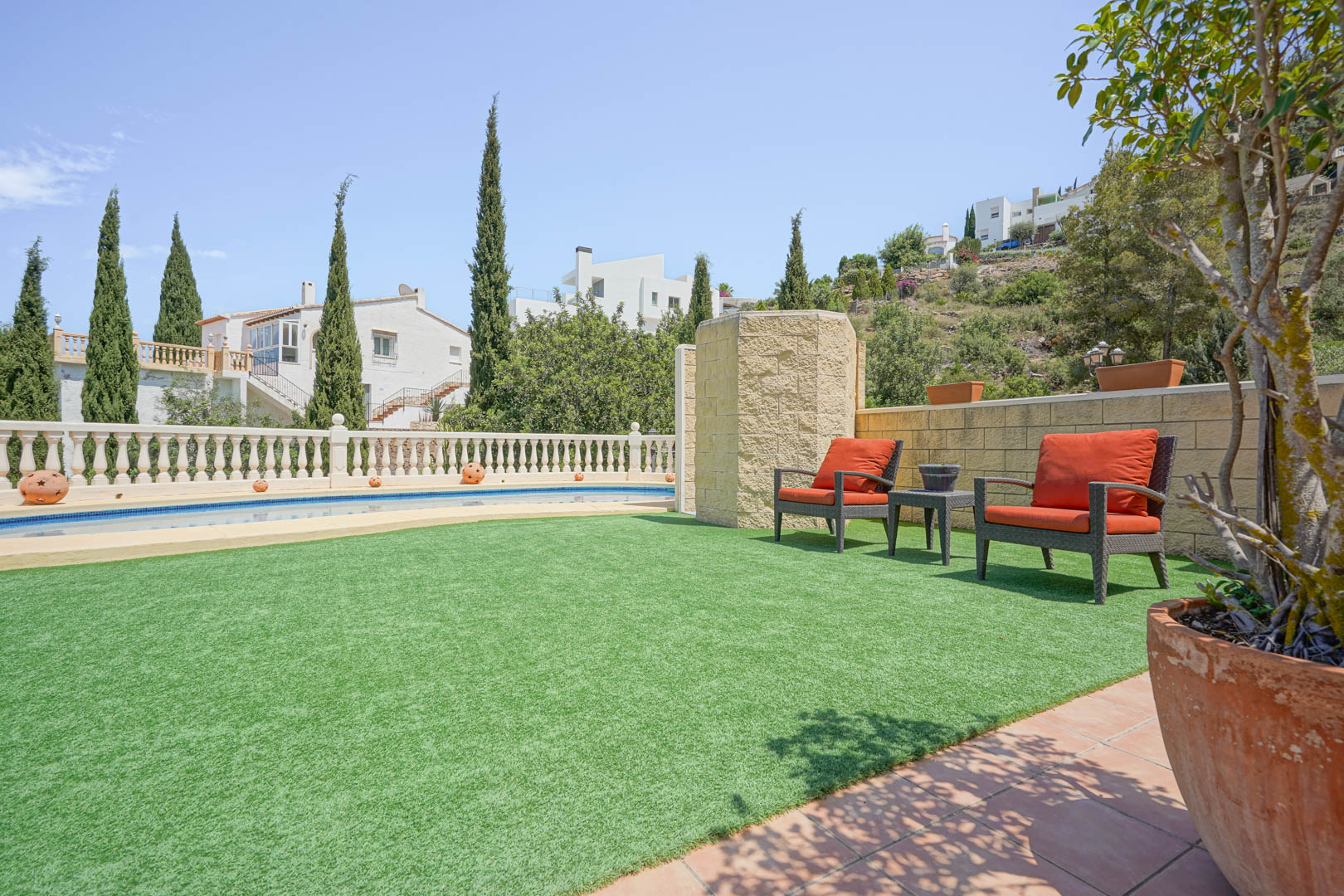Outdoor terrace featuring artificial turf, orange lounge seating, and a private swimming pool framed by a classic white stone balustrade.