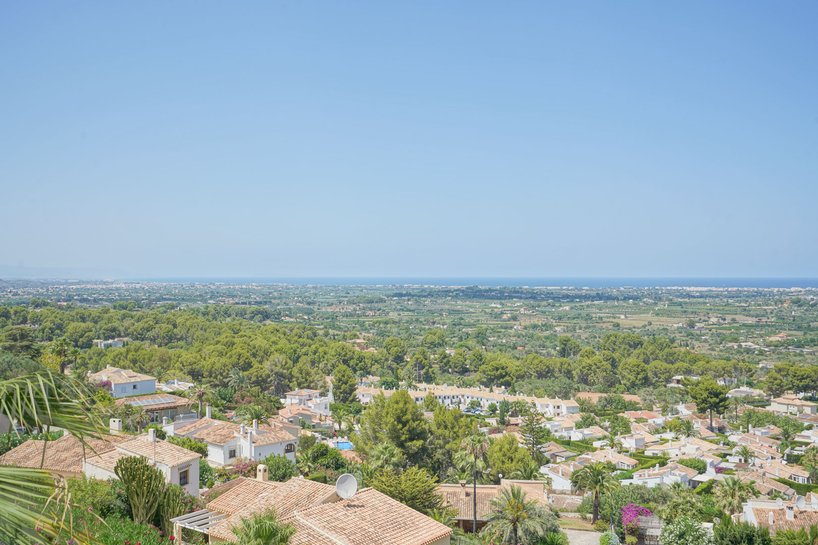 Panoramic view from the elevated terrace overlooking the valley and Mediterranean Sea, featuring lush greenery and traditional terracotta rooftops.
