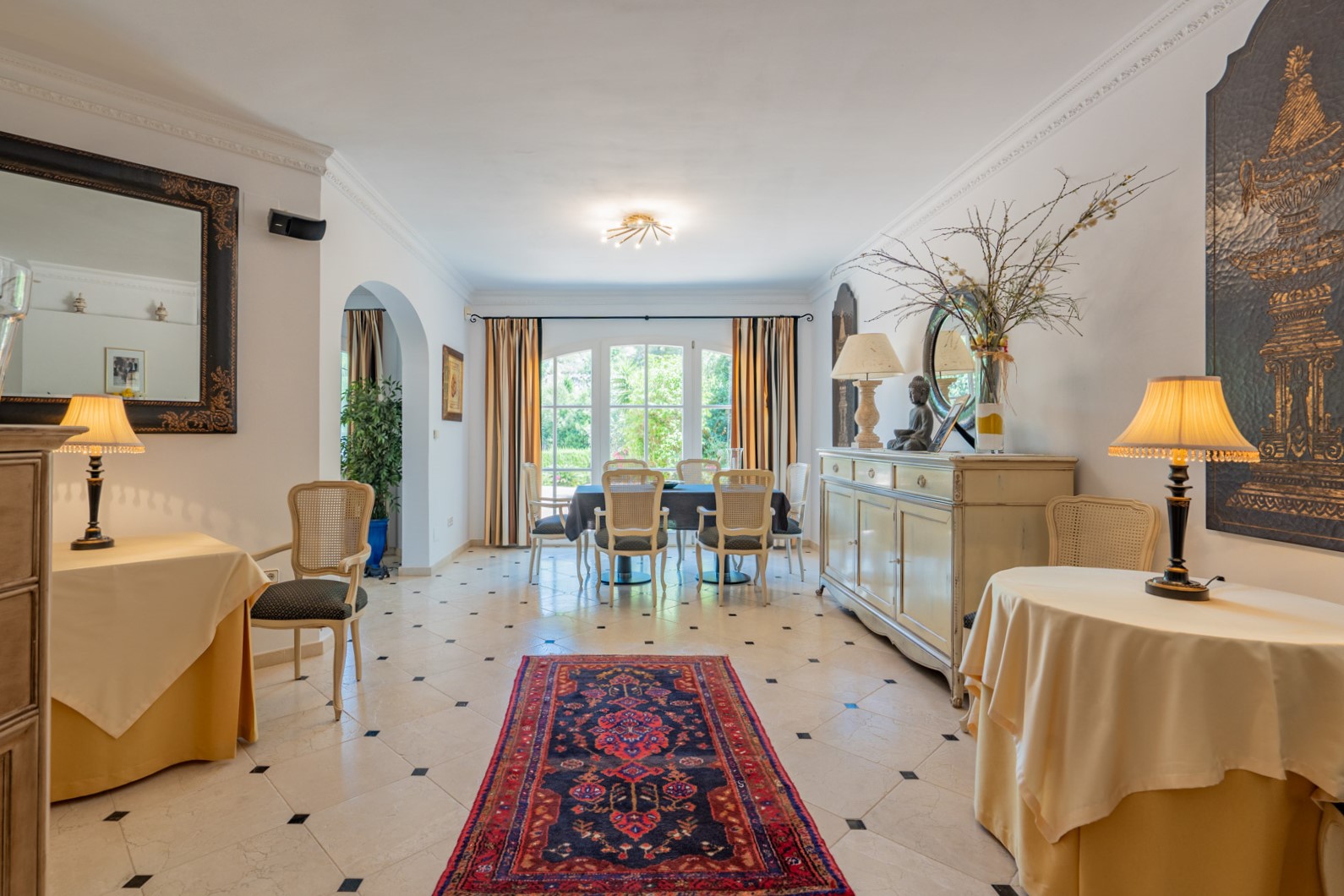 Spacious dining room featuring marble flooring with black diamond insets, classic furniture, and large arched windows providing direct access to the garden.