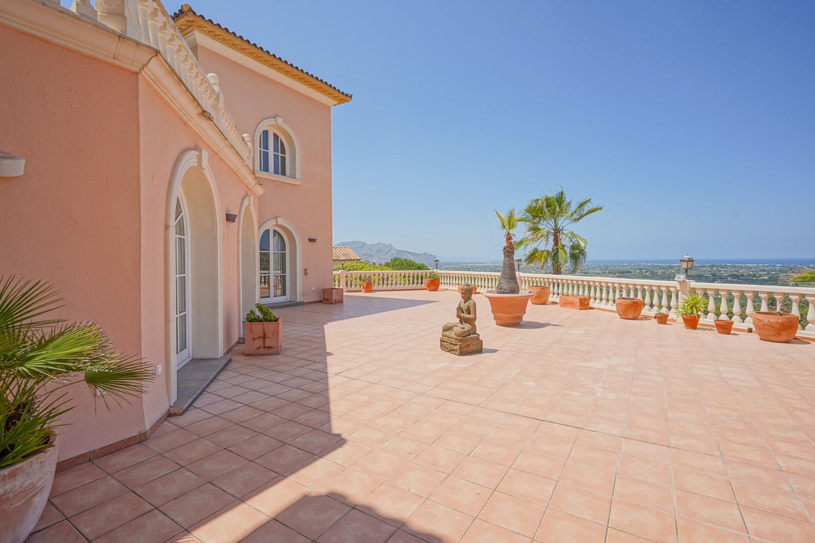 Spacious terrace with terracotta tiling and a classic balustrade overlooking the Mediterranean. The salmon facade features arched windows and decorative stone elements.