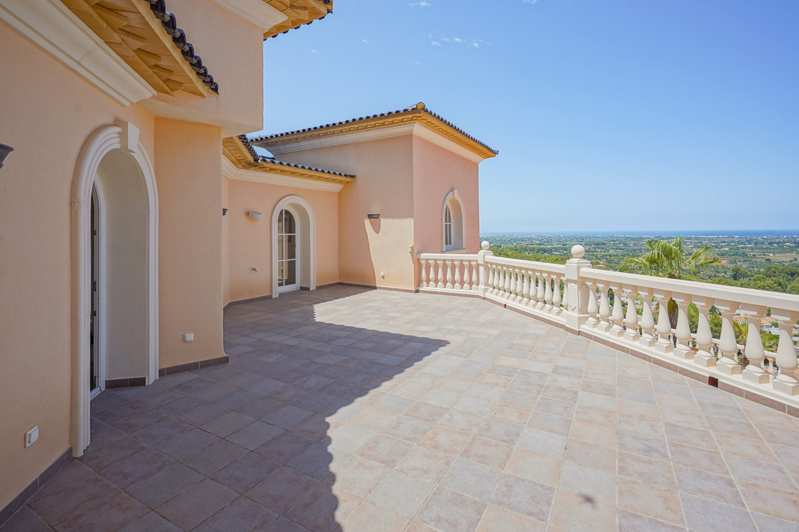 Spacious upper terrace featuring stone tile flooring, a classic white balustrade, and panoramic views of the valley and Mediterranean coastline.