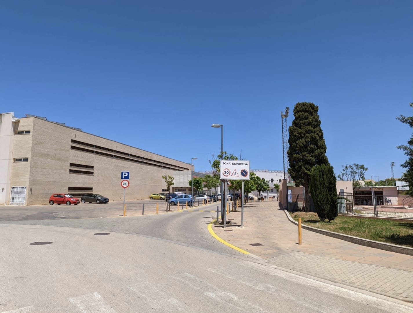 Exterior view of the access road to the Denia sports complex, featuring wide sidewalks, clear signage, and modern institutional brick buildings.