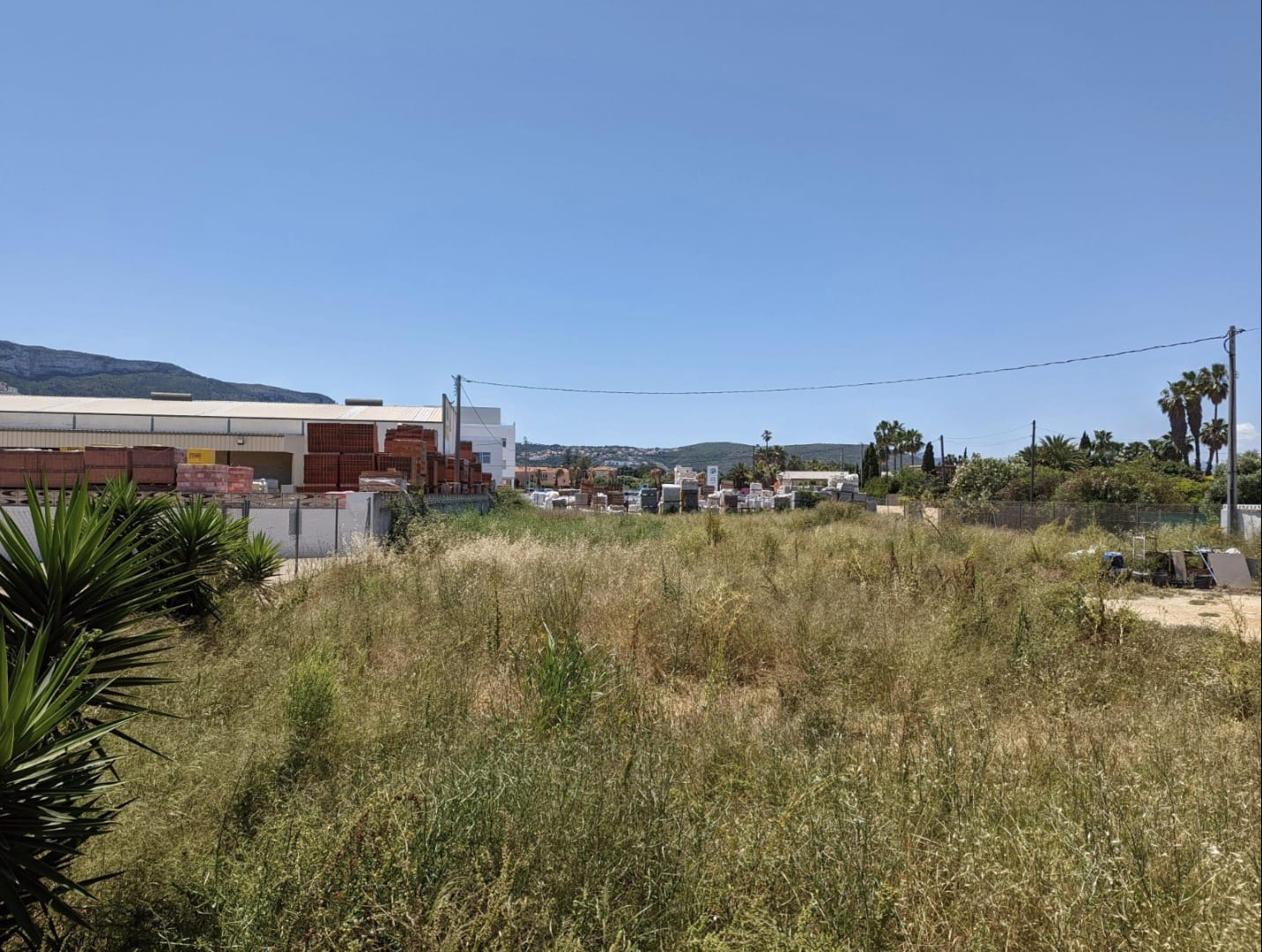 Level building plot with native vegetation and views of the Montgó mountain. The site is fenced and located adjacent to commercial facilities.