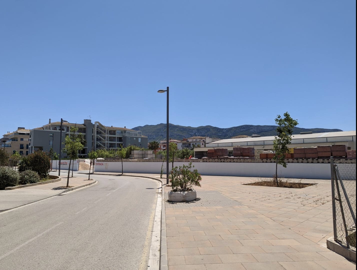 View of the urban plot with paved road access and perimeter fencing, featuring views of the Montgó mountain and proximity to residential infrastructure.