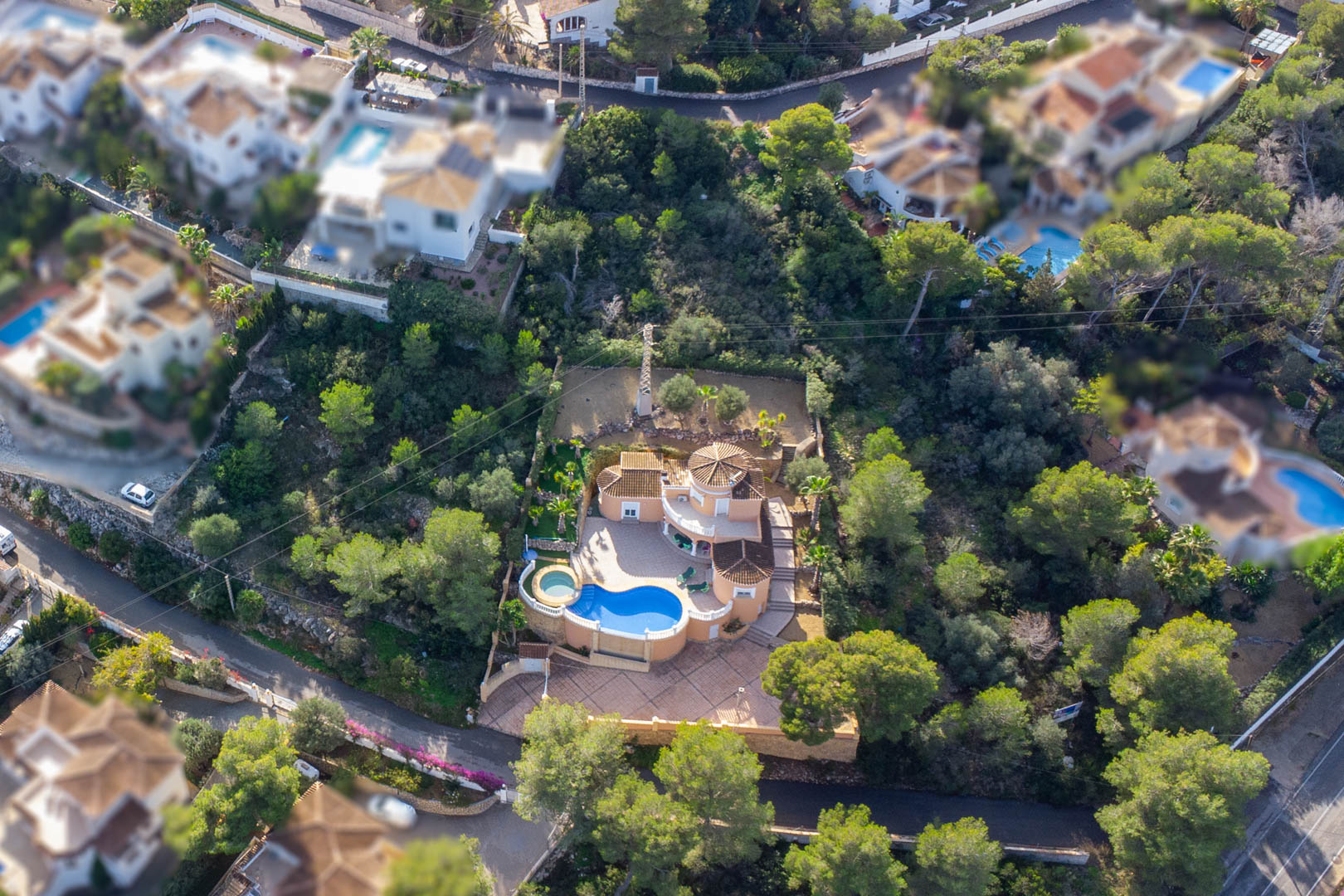 Aerial perspective of the Mediterranean villa showcasing the kidney-shaped pool, circular jacuzzi, and expansive paved terraces set within a lush pine forest.