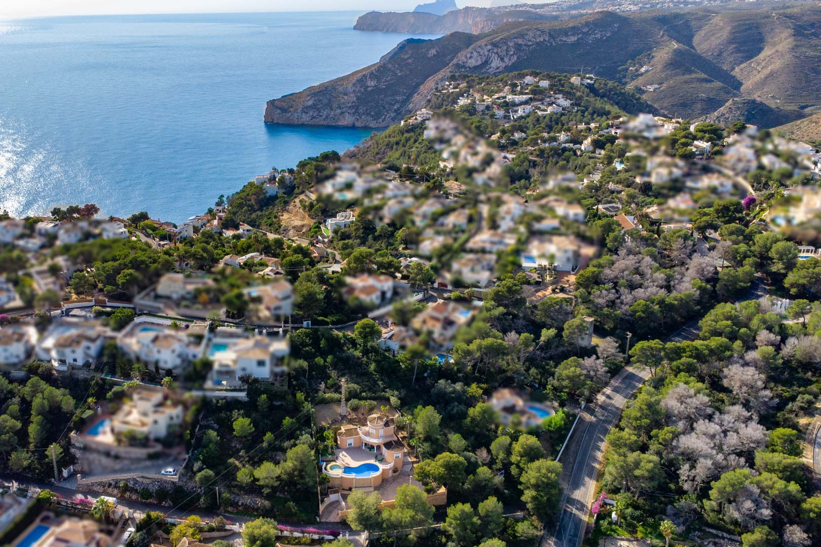 Aerial perspective of the villa featuring a curved swimming pool and integrated jacuzzi, set against a backdrop of Mediterranean pines and the Javea coastline.