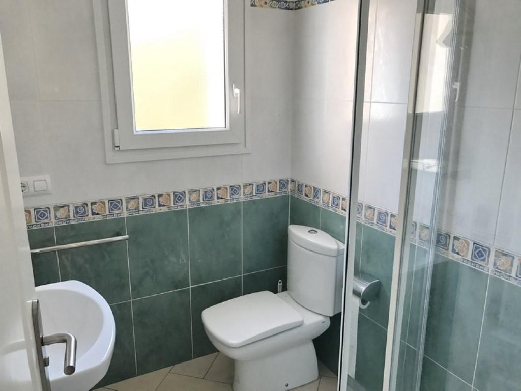 Bathroom featuring white ceramic fixtures, green and white wall tiling with decorative borders, and a glass-enclosed shower unit under natural light.