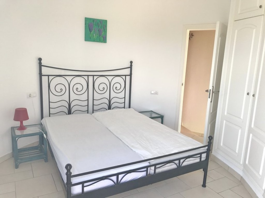 Bedroom featuring a black wrought iron bed frame, built-in white wardrobes, and light tiled flooring. The space includes glass-topped side tables and neutral wall tones.