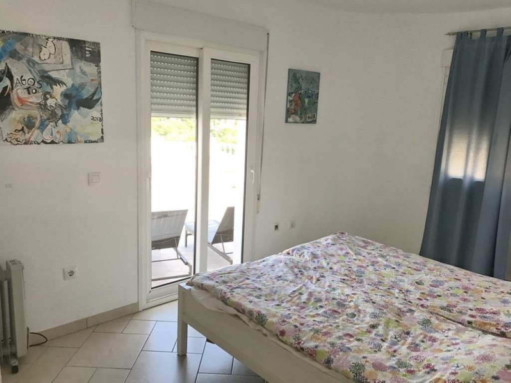 Bright bedroom featuring white tiled floors and direct access to a private terrace with sun loungers through sliding glass doors.