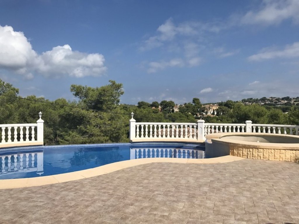 Curved swimming pool and elevated jacuzzi with stone cladding, featuring a paved terrace and white balustrade overlooking the pine-covered hills.