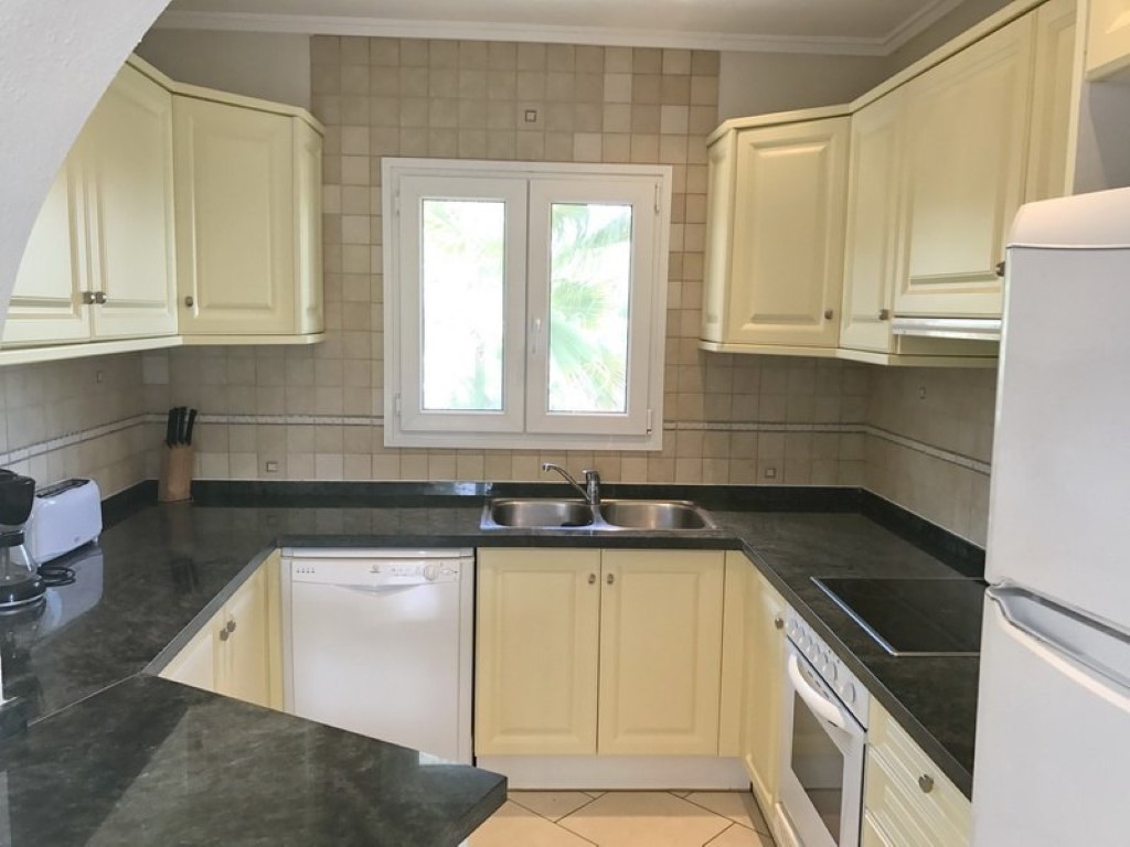Fully equipped U-shaped kitchen with cream cabinetry, dark granite countertops, a double stainless steel sink, and integrated white appliances.