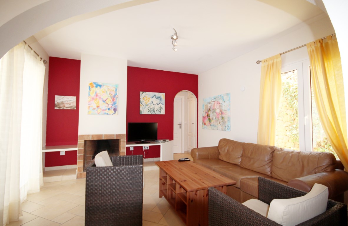 Living room featuring a red accent wall, brick fireplace, and leather seating. The space includes a wooden coffee table, tiled flooring, and natural light.