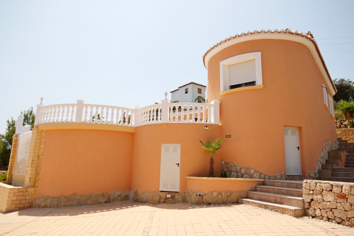 Mediterranean villa exterior featuring a terracotta-toned circular tower, white balustrades, and a paved patio with natural stone accents.