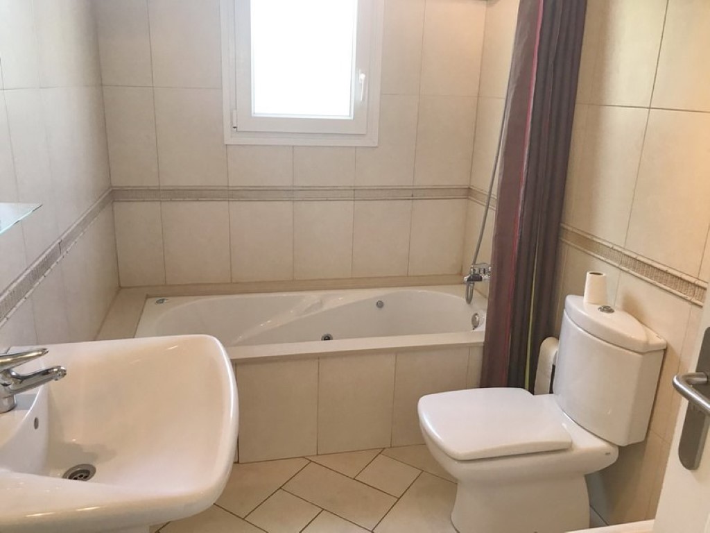 Modern bathroom featuring a built-in jetted bathtub, white ceramic sink, and matching toilet. Neutral beige wall tiles with a decorative border and diagonal floor tiling.