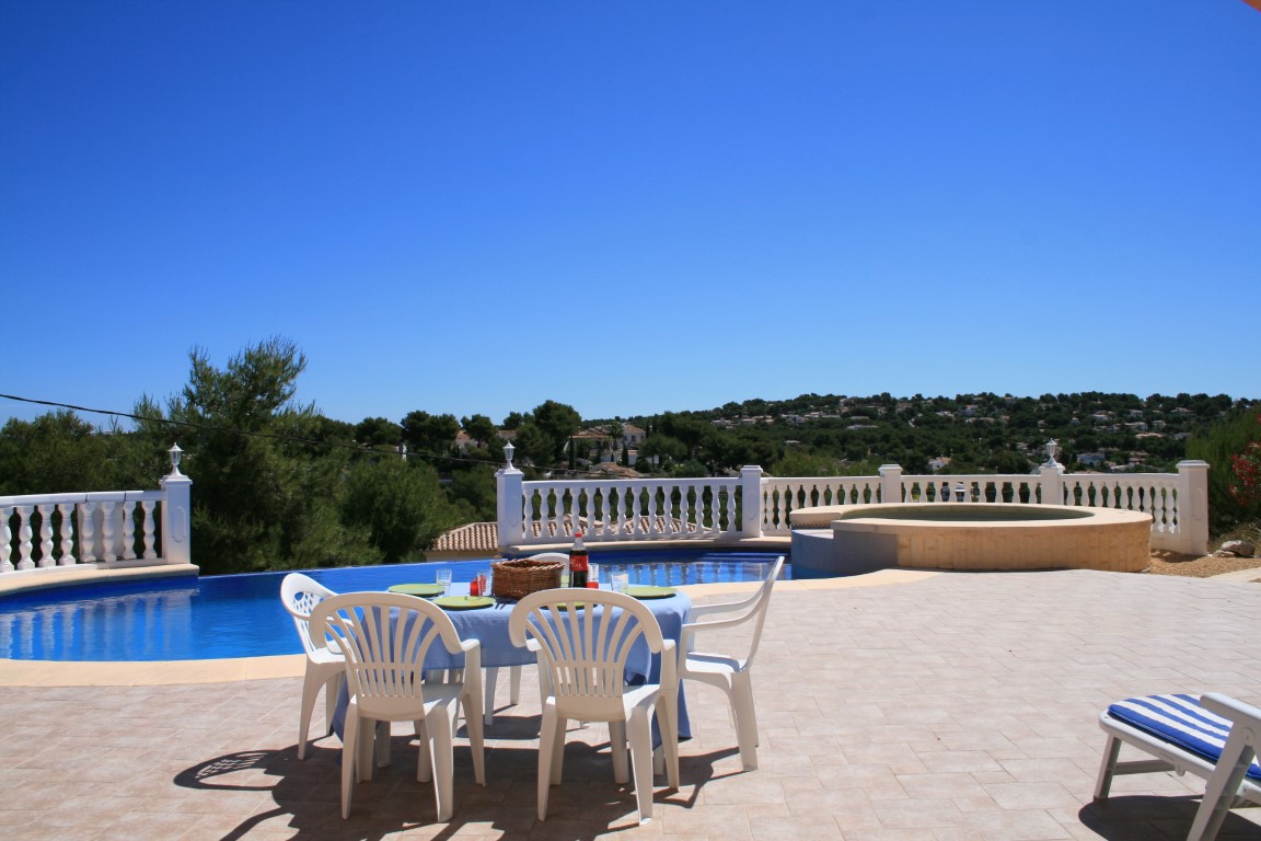 Spacious outdoor terrace featuring a curved swimming pool, integrated circular jacuzzi, and a dining area with panoramic views of the Javea hills.