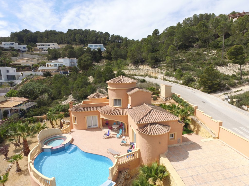 Aerial view of the Mediterranean villa featuring a terracotta facade, a curved swimming pool with integrated jacuzzi, and a spacious sun terrace overlooking pine-covered hills.