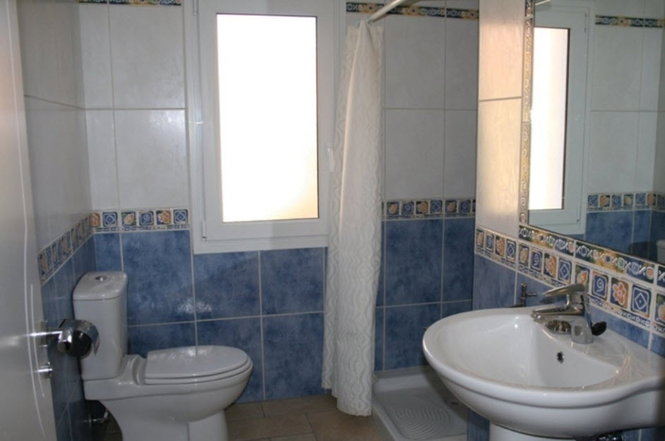 Bathroom featuring blue and white tiling with a decorative border, a pedestal sink, a shower tray with a curtain, and a frosted window for natural light.