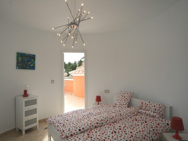 Bright bedroom featuring a curved wall, modern starburst chandelier, and direct access to a private terrace. Includes white furniture and tiled flooring.