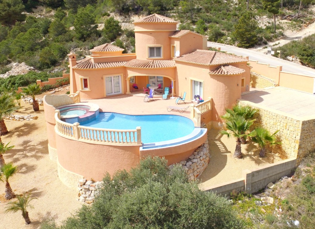 Exterior view of the Mediterranean villa featuring a curved infinity pool with integrated jacuzzi, terracotta facade, and palm-lined terrace.