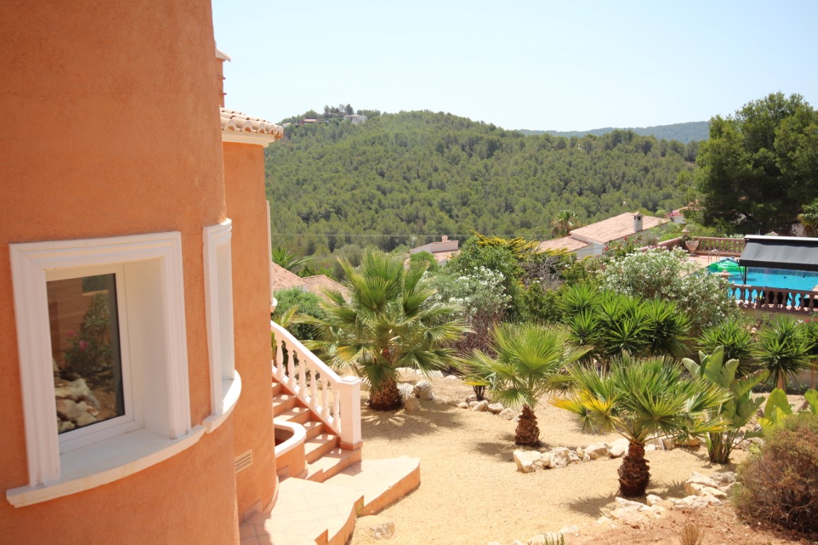 Exterior view of the terracotta-toned curved facade featuring a low-maintenance Mediterranean garden with palms and panoramic views of the forested valley.