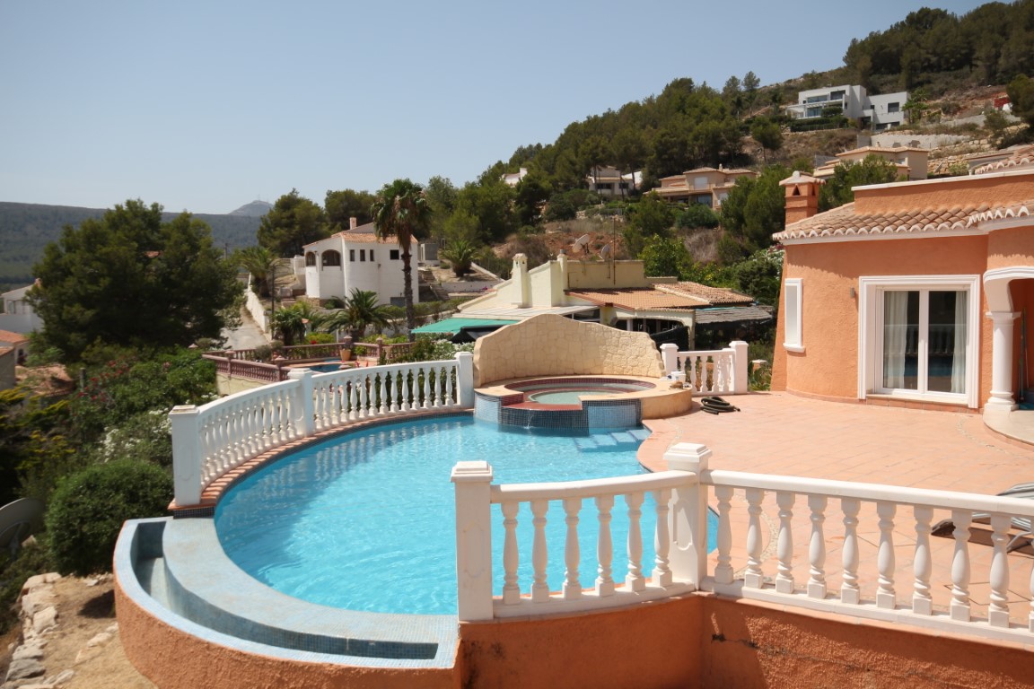 Solarium terrace featuring a curved infinity pool with blue tiling, an integrated jacuzzi with a stone feature wall, and classic white balustrades.
