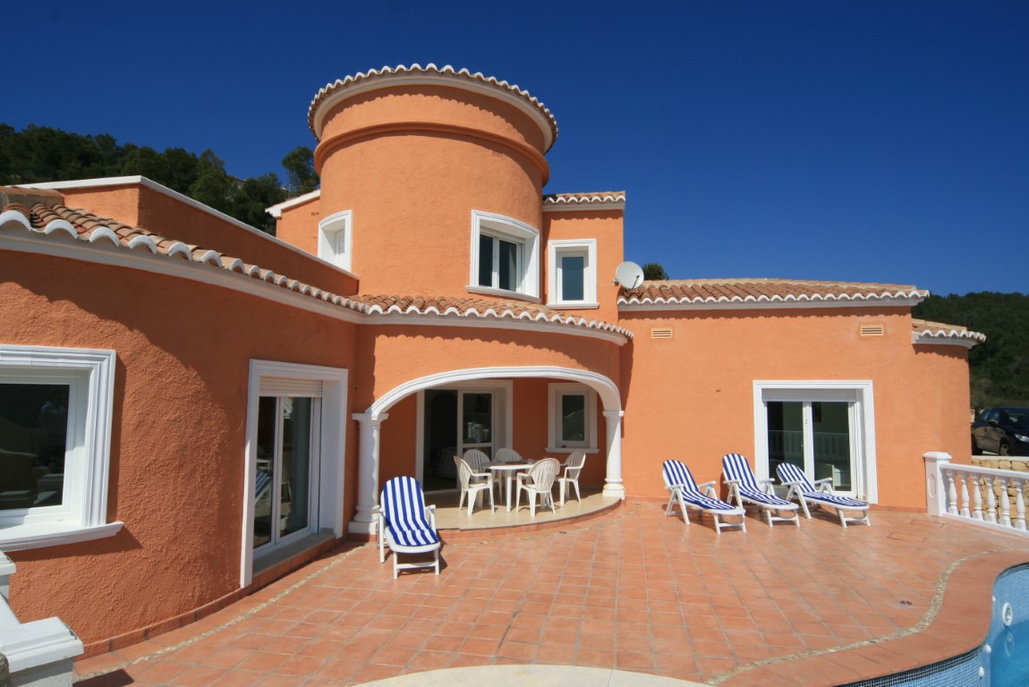 Terracotta-toned Mediterranean villa exterior featuring a circular tower, expansive tiled terrace with striped loungers, and an arched porch for shaded dining.