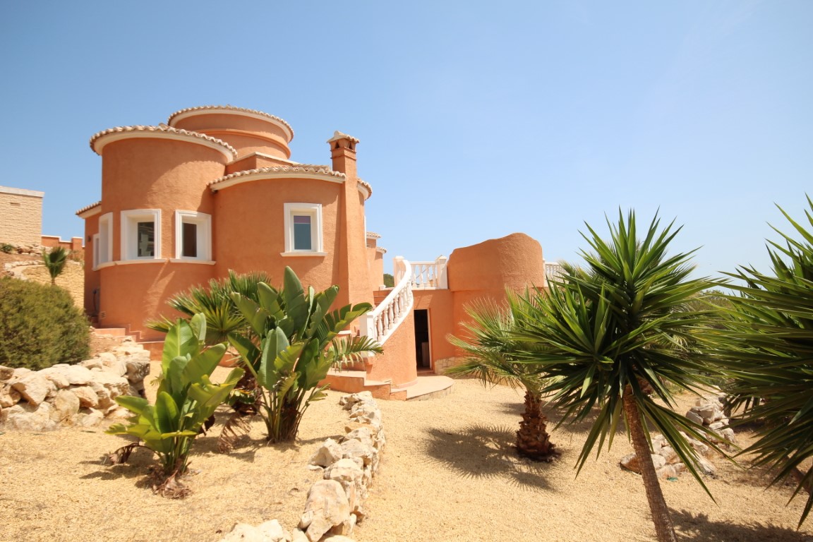 Terracotta-toned villa featuring rounded architectural volumes, an exterior white balustrade staircase, and a gravel garden with Mediterranean palms.