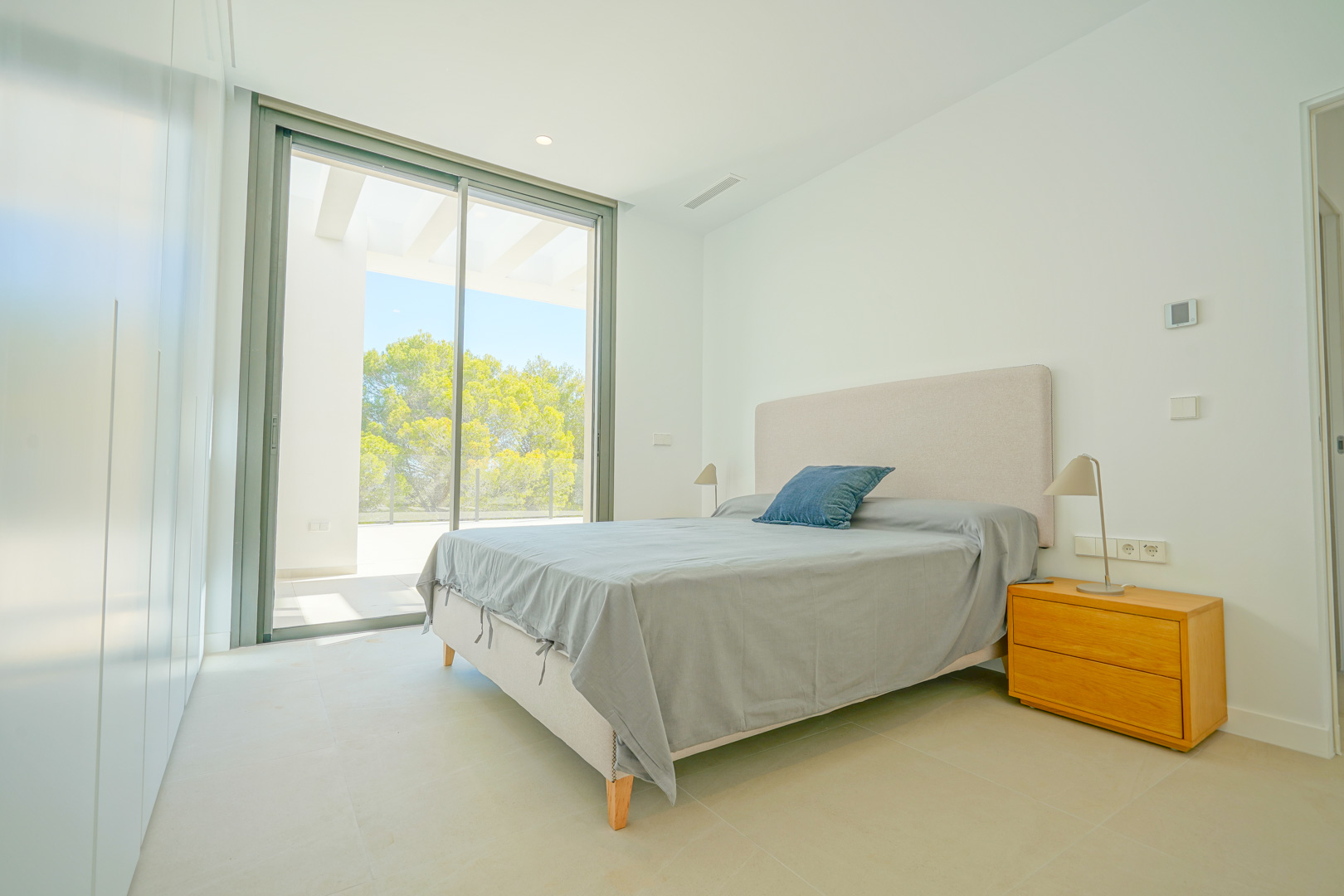 Bright bedroom featuring floor-to-ceiling sliding doors, direct terrace access under a pergola, minimalist built-in wardrobes, and views of the forest.