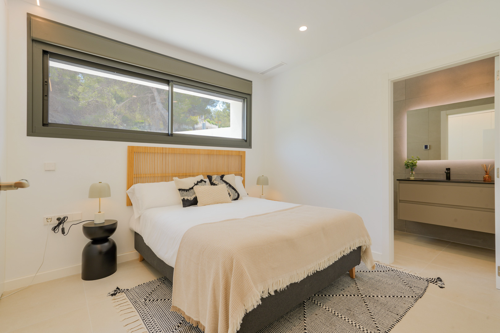 Double bedroom featuring a wooden slatted headboard, large horizontal window with forest views, and an integrated en-suite bathroom with a backlit mirror.