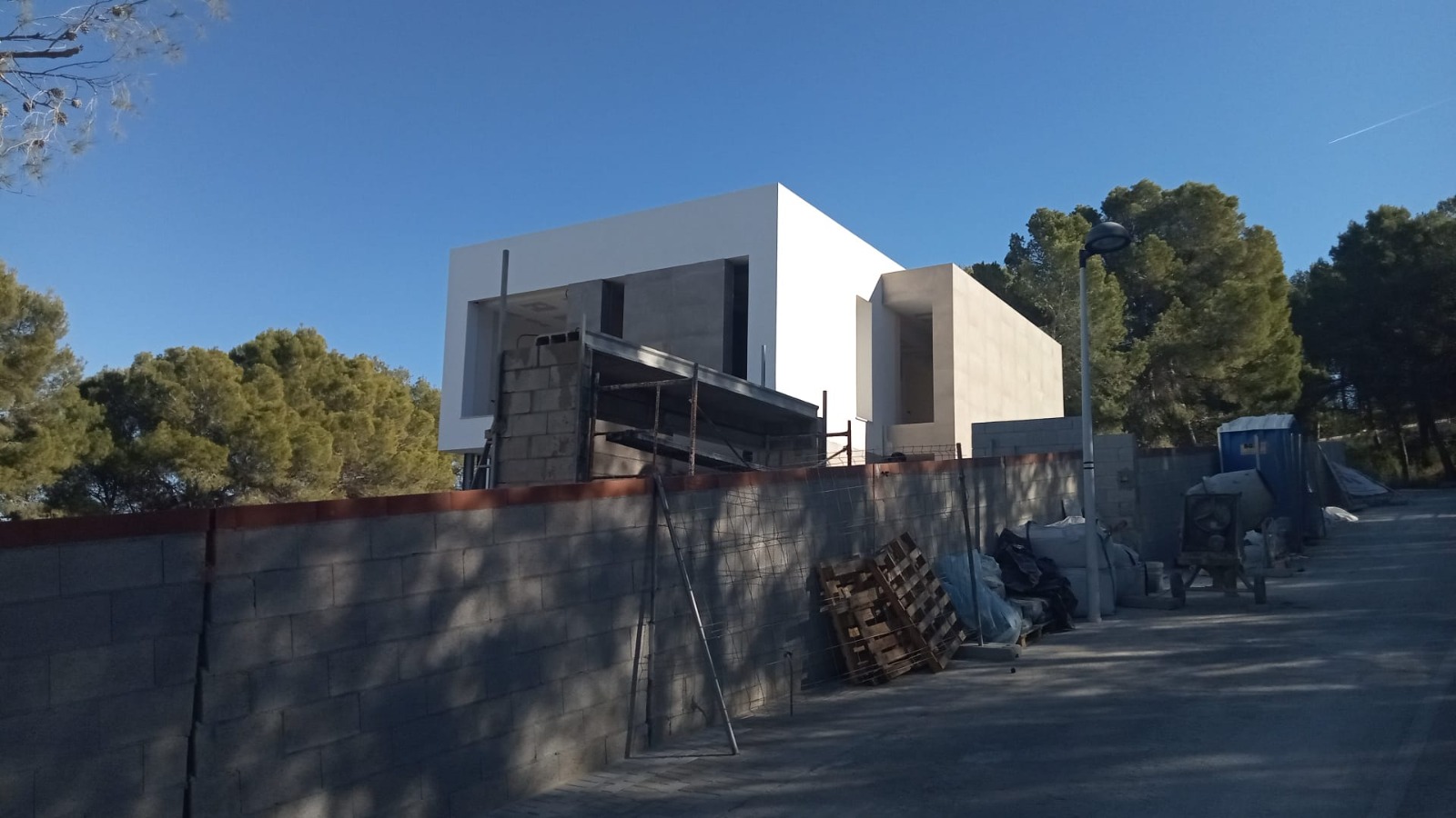 Exterior view of the modern villa during construction, featuring minimalist cubic architecture with white and stone facades in a quiet wooded setting.