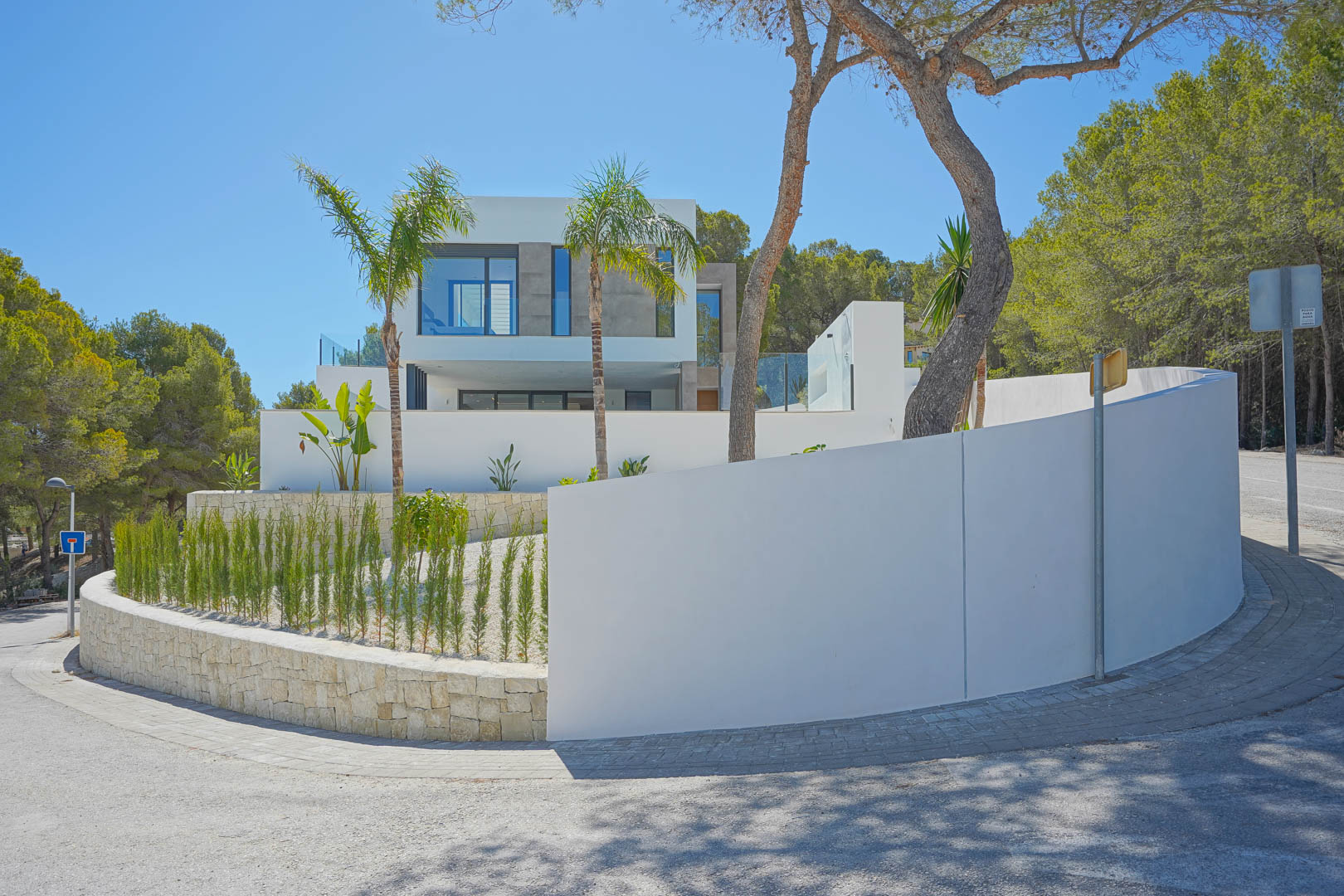 Exterior view of the modern villa featuring white facades, curved perimeter walls, and Mediterranean landscaping with cypress and palm trees.