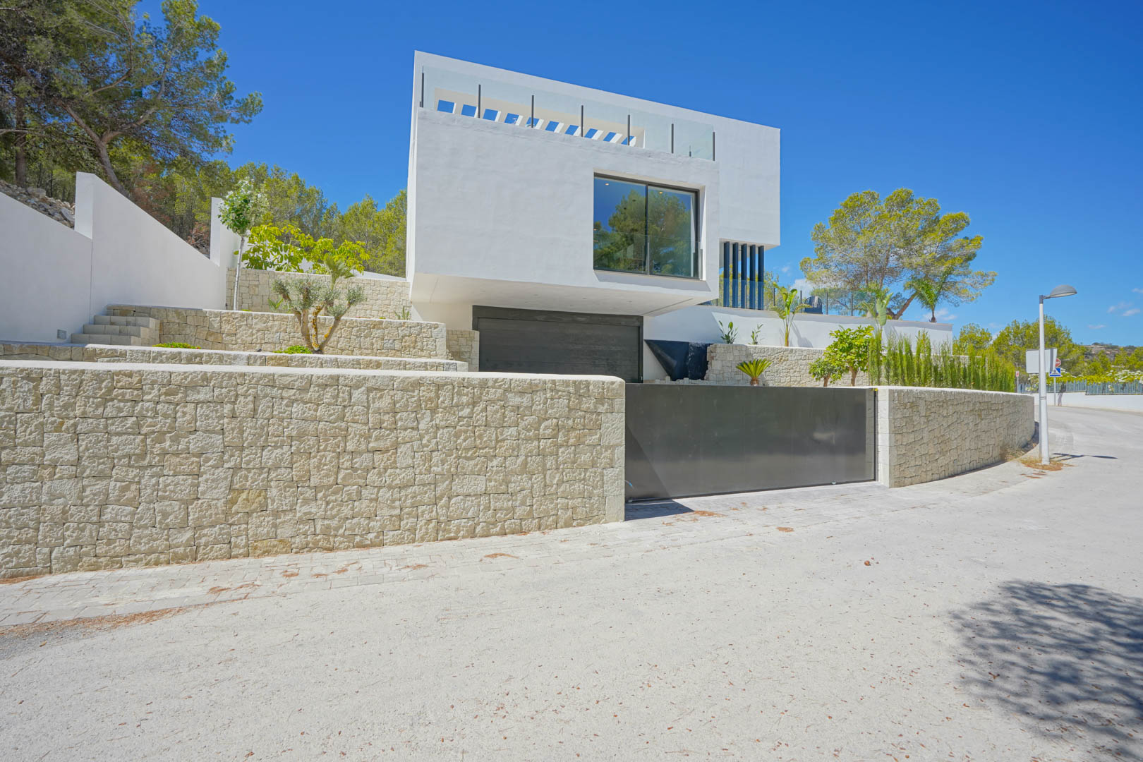 Modern exterior facade featuring natural stone retaining walls, a double garage entrance, and terraced Mediterranean landscaping.