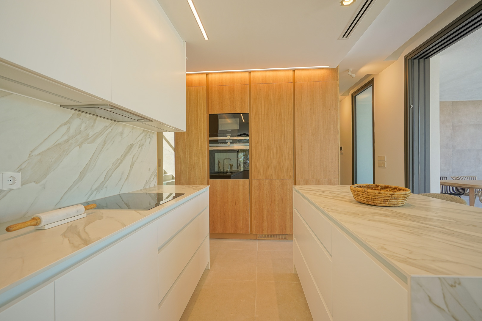Modern kitchen featuring veined marble countertops, minimalist white cabinetry, and a wood-paneled wall with integrated appliances and recessed linear lighting.