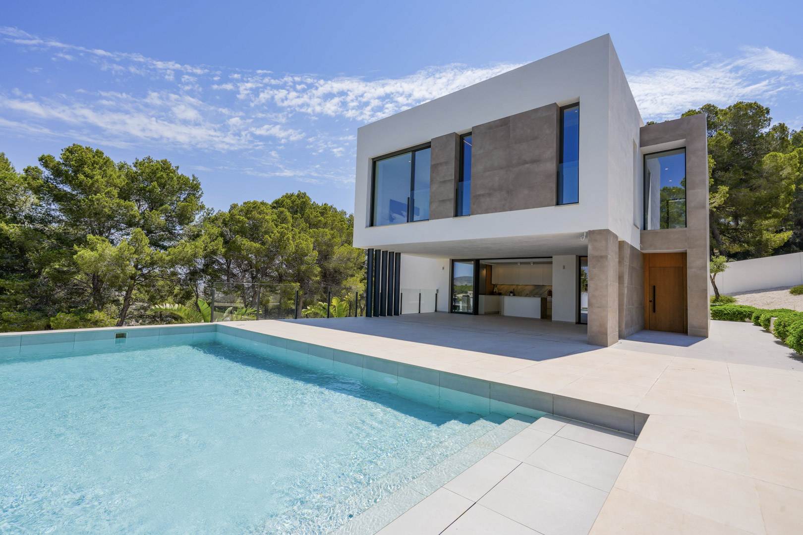 Modern villa exterior featuring an infinity pool and expansive stone terrace, showcasing clean architectural lines set against a backdrop of Mediterranean pines.