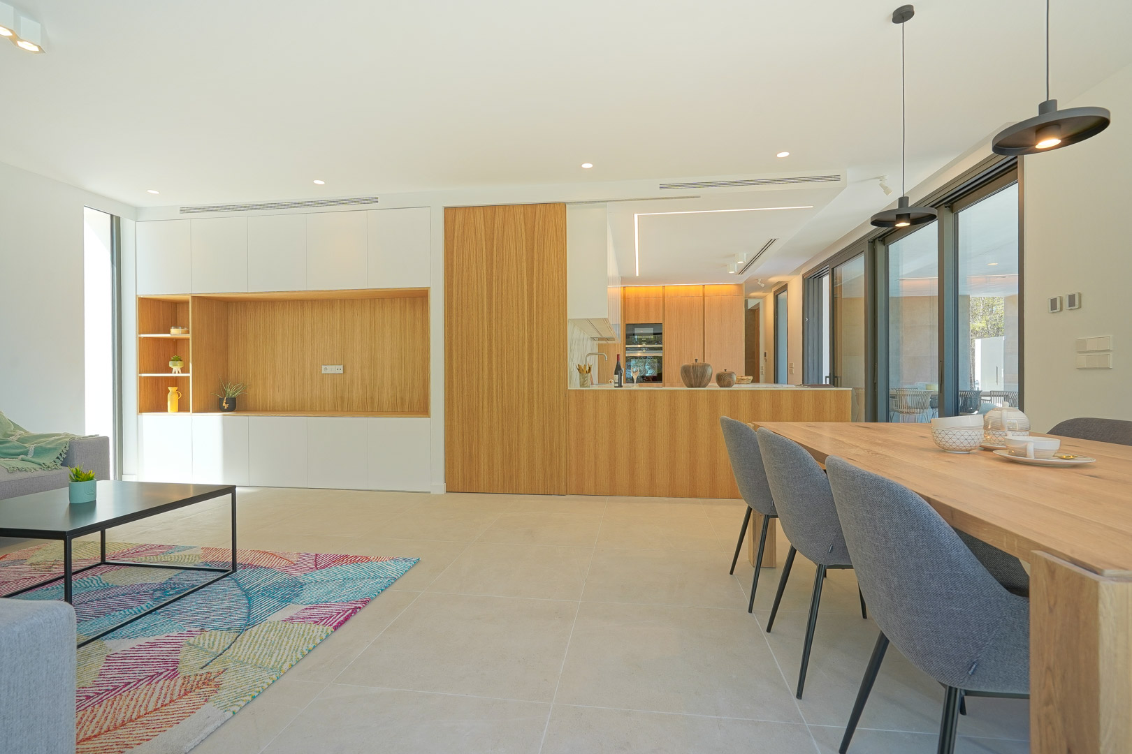 Open-plan living and dining area featuring integrated wood cabinetry, minimalist furniture, and large sliding doors providing abundant natural light.