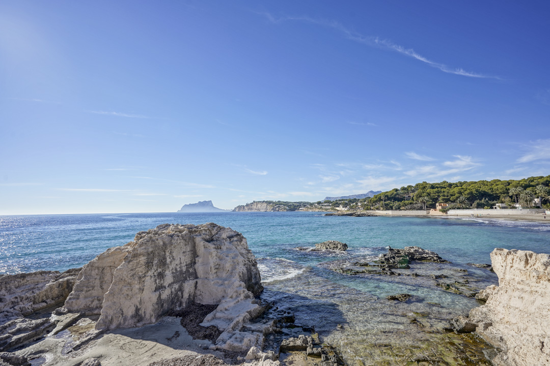 Panoramic views of the Mediterranean Sea featuring the Peñón de Ifach on the horizon from the rocky coastline near Moraira.