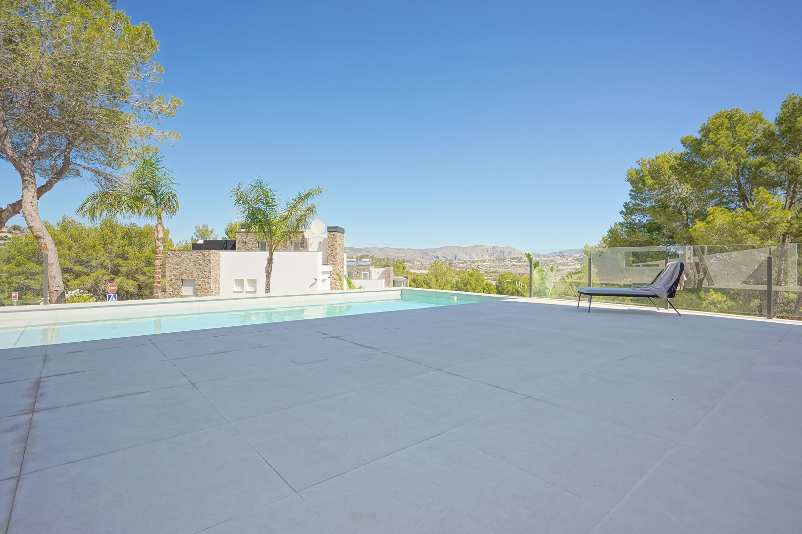 Spacious terrace featuring large-format tiling, an infinity pool, and a glass balustrade offering panoramic views of the valley and pine forest.