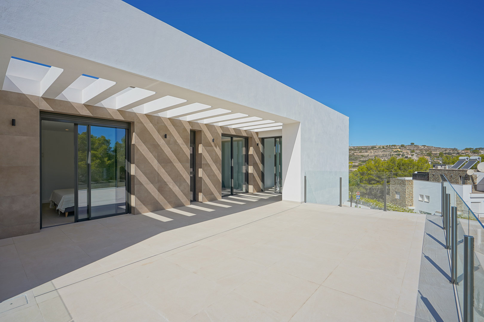Upper-floor terrace featuring a white pergola, glass balustrades, and direct bedroom access through large sliding glass doors.