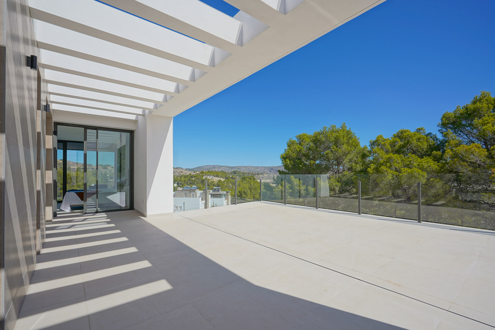Upper-level terrace featuring a white pergola, glass balustrades, and expansive views of the surrounding wooded landscape and hills.
