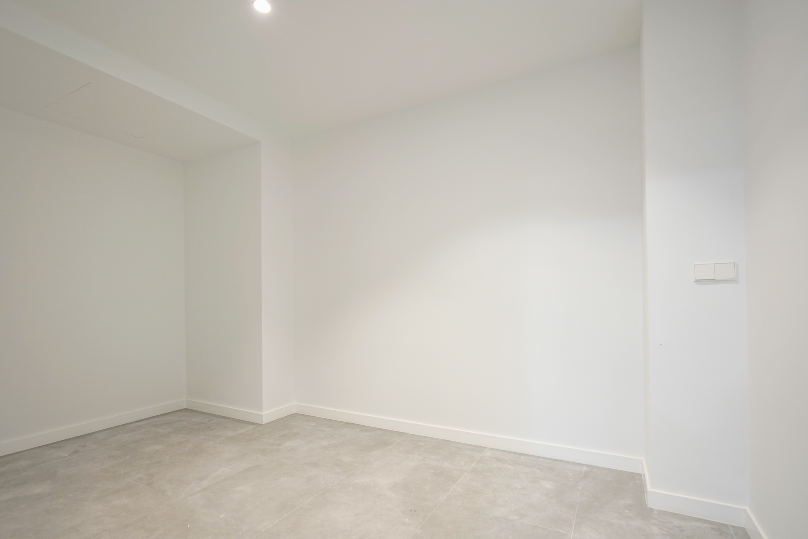 Versatile interior space featuring white walls, grey tiled flooring, and recessed lighting, suitable for storage or technical use on the ground floor.