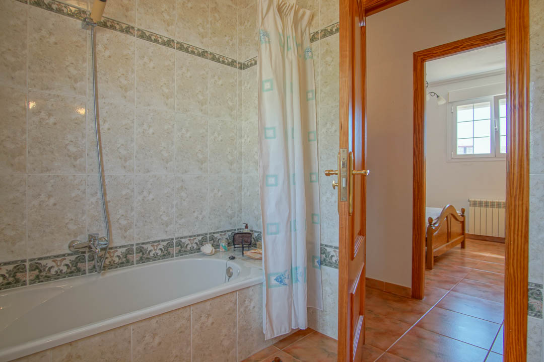 Bathroom featuring a built-in bathtub, decorative tile borders, and solid wood door frames leading to a bedroom with natural light.